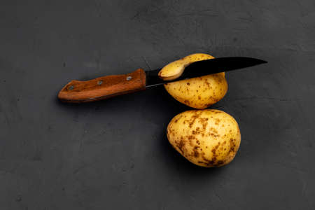 Potato and knife. Peeling potatoes. Dark background. Preparing for cooking potatoes.の写真素材