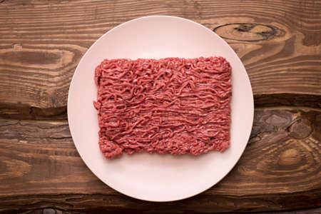 Fresh minced meat on a plate on a wooden background for cooking.