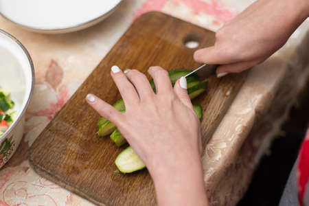 Woman cuts cucumbers on the cutting board.の写真素材