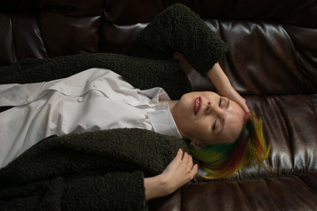 A woman with multi-colored hair is lying on a leather sofa.の写真素材