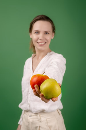Beautiful middle-aged woman in a white shirt with apples on a green background. The concept of diet, healthy food, vegetarianism.の写真素材
