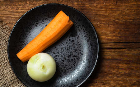 Raw peeled onions and carrots on a black plate on a wooden background.の写真素材