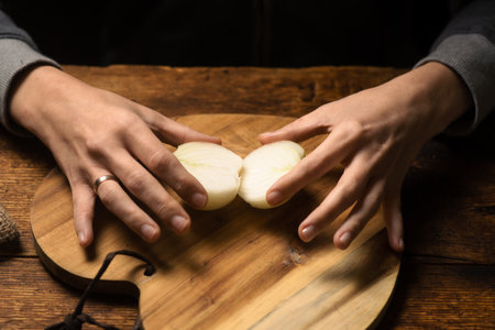 halves of a raw onion in the hands of a woman on a wooden background.の写真素材