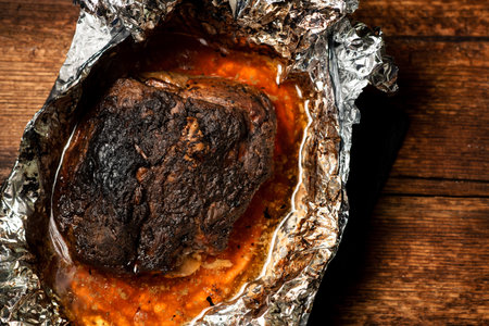 A large piece of baked meat with spices wrapped in foil in the oven.