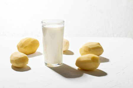 Potato milk alternative. A glass of milk and a raw potato on a white background.の写真素材