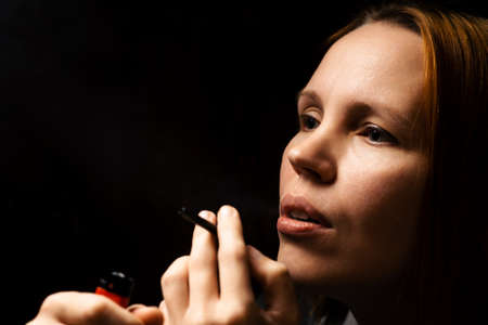 Woman smokes marijuana, cannabis through a device on a black background.