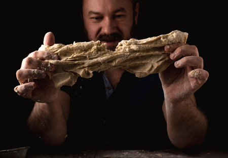 Unshaven man kneading dough on a black background.