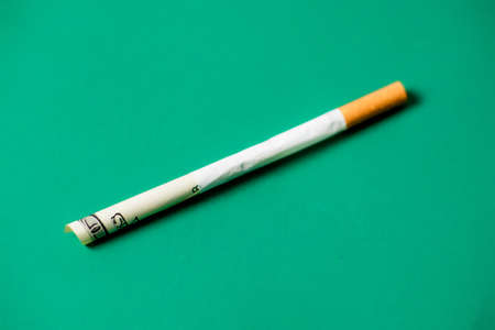 smoking and money. Rolled up dollar bill in a cigarette. green background. The high cost of smoking...