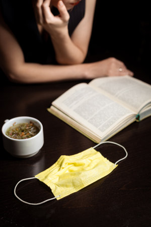 Cafe and pandemic. Medical mask, cup and open book. dark background. End of quarantine.