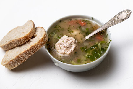 Vegetable soup with meatballs in a plate on a white background. Two slices of bread side by side.の写真素材