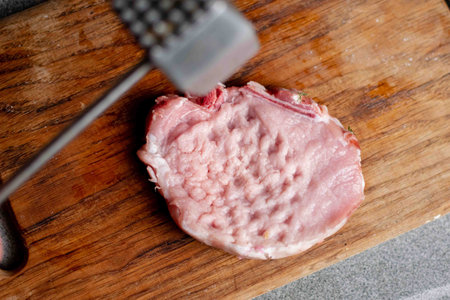 Beating meat with a hammer on a wooden board. Cooking pork chop.の写真素材