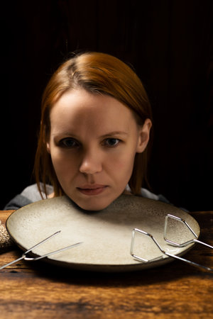 Female head on a plate on a dark background. Fear of diet, apathy concept.の写真素材