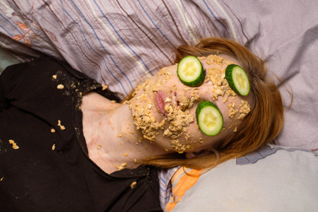 A woman makes a cosmetic mask at home from oatmeal on her face and cucumber. Anti-aging treatments, skin care concept.の写真素材