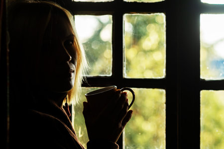 Dark profile of a woman with a cup in her hand near the window. morning coffee.の写真素材