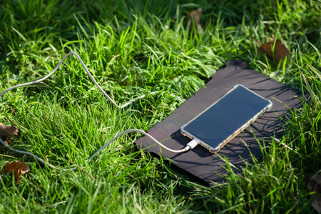 Portable solar battery and mobile phone on green grass. Charging electronic gadgets on a hike, during outdoor recreation. Ecological energy concept.の写真素材