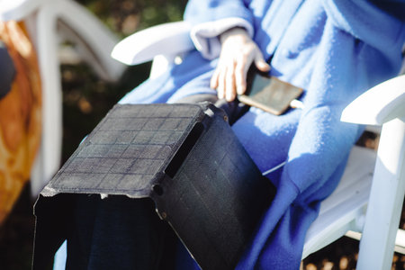 A portable solar battery rests on the legs of an unrecognizable woman. Ecological alternative energy concept.の写真素材