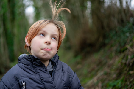 Young funny positive boy fooling around. A boy in a warm jacket blows his hair outdoors....