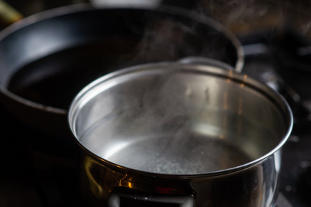 A pot of boiling water on a kitchen stove. Kitchen utensils are nearby.