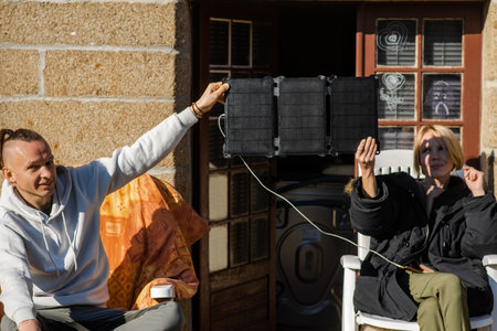 A man and a woman resting hold a portable solar battery. Charging mobile gadgets in nature without electricity. Alternative energy source concept.の写真素材