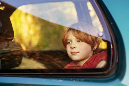 A young boy of eight or ten years old sits in a car behind glass. Car travel, train concept. red-haired boy.の写真素材