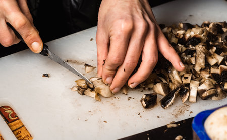 Sliced champignon mushrooms on a cutting board. Women's hands cut mushrooms with a knife.