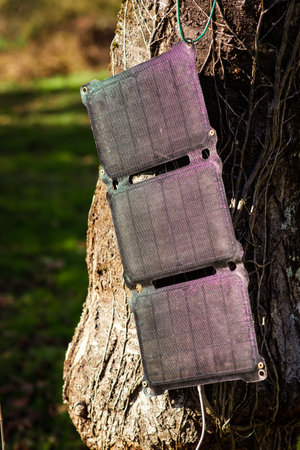 A portable solar panel hangs on a tree in the sun. Charging electronic gadgets on a hike, during outdoor recreation. Ecological energy concept.の写真素材