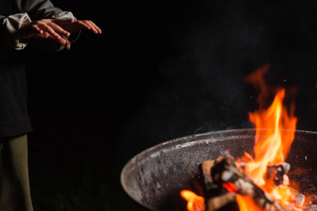 The child's hands warm themselves near the fire of the barrel in the dark. Homeless, emigrant, beggar concept.の写真素材