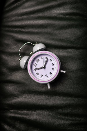 Time management, deadline concept. Alarm clock lies on dark leather background of sofaの写真素材