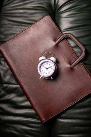 Time management, deadline concept. Alarm clock on folder for papers on dark backgroundの写真素材