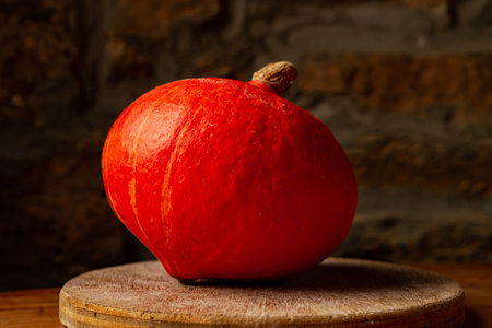 Small orange pumpkin on wooden surface against window background.の写真素材