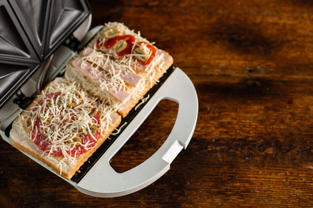Cooking sandwiches with cheese, sausage, olives in a sandwich maker on a wooden background.の写真素材