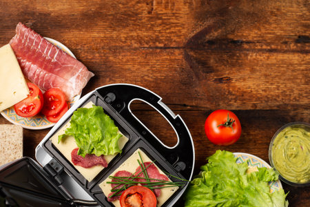 Cooking sandwiches with different fillings. Sandwich maker and various ingredients on wooden background. Place for text.の写真素材