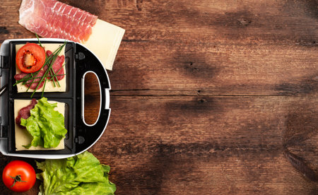 Cooking sandwiches with different fillings. Sandwich maker and various ingredients on wooden background. Place for text. banner.の写真素材