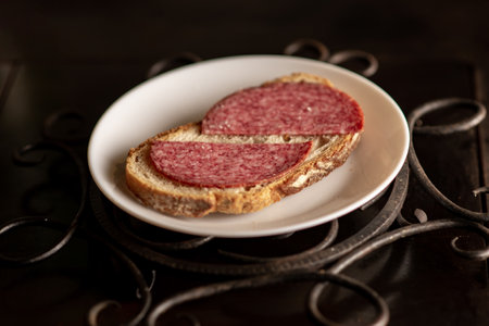 Bread with salami on a white plate on a dark background. simple sandwich.の写真素材