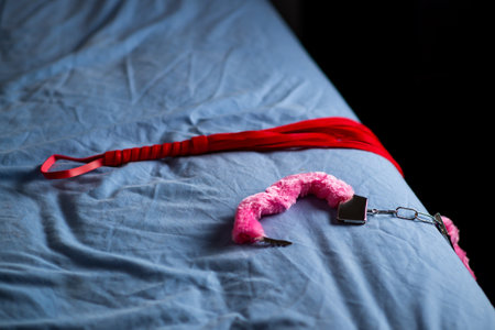 Handcuffs with red fur and a whip. Devices for love games on the bed.