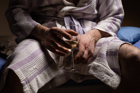 Man and alcoholism. An unrecognizable man in a bathrobe holds a glass of wine. Drink alcohol to fall asleep before bed.の写真素材