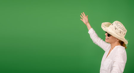 Cheerful smiling woman in a hat and sunglasses in a white shirt on a green background. Banner. Place for your text.の写真素材