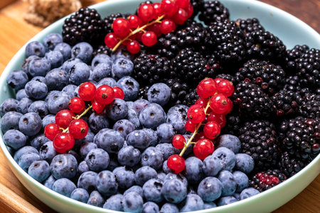 Different mixture of berries - blueberries, blackberries and red currants in a plate on a wooden background. Fruit, berry background.の写真素材