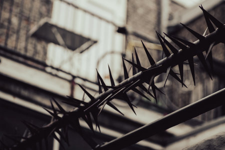 Tricky depression concept. A barrier with sharp long metal spikes against the background of a building in blur. Heaviness, negative.の写真素材