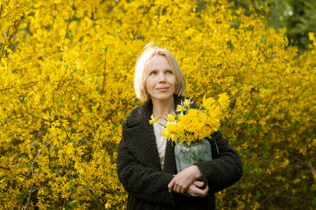 A woman looks into the distance with a bouquet of yellow flowers on a background of yellow flowers. spring mood.の写真素材