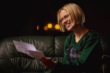 Joyful letter woman holds. Attractive middle-aged woman with a happy expression reads pleasant news from a letter at home.の写真素材