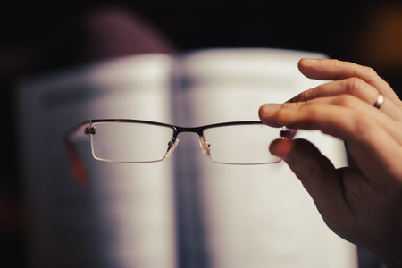 Glasses in a female hand. The concept of poor eyesight, reading books, learning.の写真素材