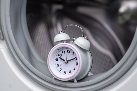 time and washing machine. Waiting, washing duration concept. Open door of washing machine and alarm clock.の写真素材