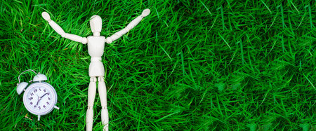 Time for rest, freedom concept. The figure of a man and an alarm clock on the green grass. Banner, place for text.の写真素材