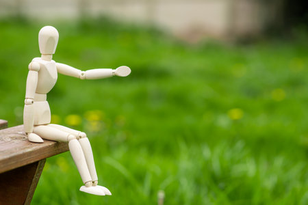 Waiting, loneliness concept. The figure of a man sits on a bench against a background of green grass. Place for text.の写真素材
