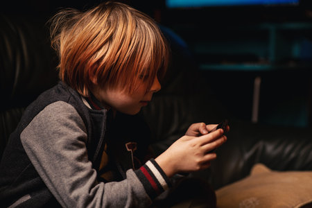 A young boy is playing on the phone. A boy of nine and ten plays or reads on a mobile phone.の写真素材