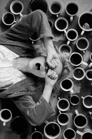 A woman yawns surrounded by many cups of coffee. Deadline, overtime concept. Desire to sleep after...