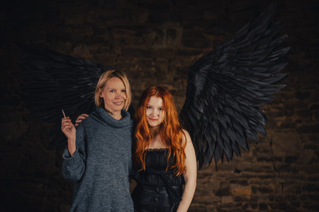 Red-haired girl with black angel wings and a woman smokes in a dark room.の写真素材