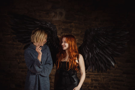 A girl with black angel wings and a woman with a cigarette laugh on a dark background.の写真素材