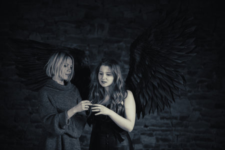 Cigarette taste. A woman passes a cigarette to an angel with black wings and red hair. Black and white image.の写真素材